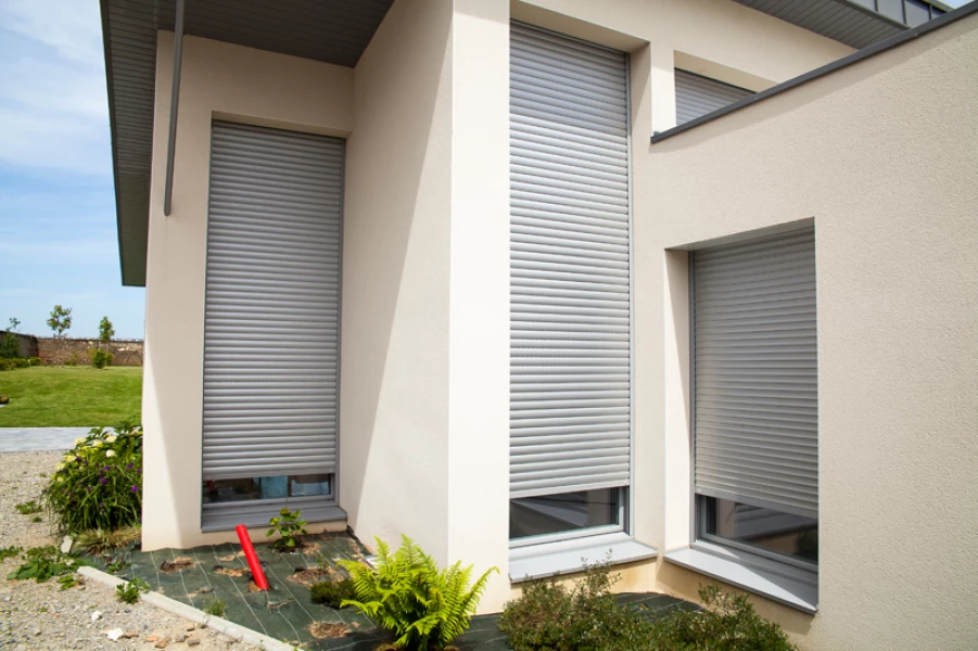 Trois volets roulants gris sur une maison blanche.